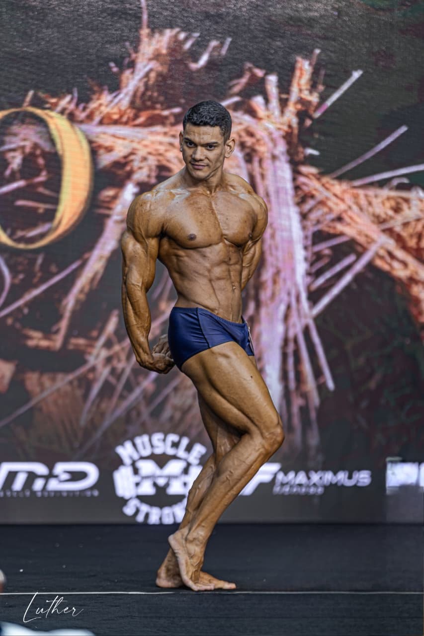 Wellbert Bianchi de perfil no palco, em pose de peitoral lateral.
